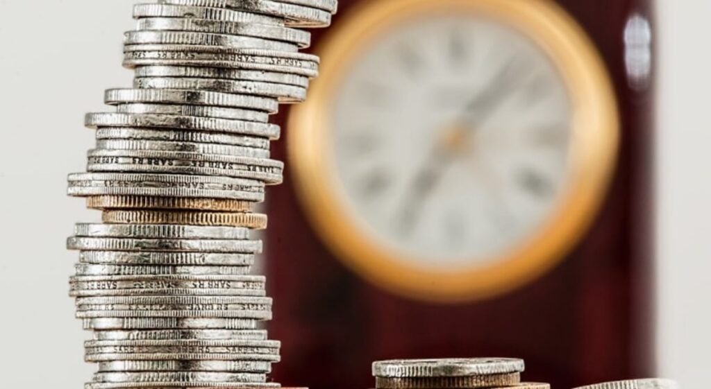 Stack di monete e un orologio che simboleggiano la gestione del tempo e la capitalizzazione nel trading online con il Trailing Stop Loss (TSL)