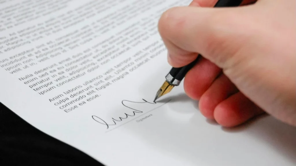 Primo piano di una mano che firma un modulo per la dichiarazione dei redditi e la detrazione delle spese funebri