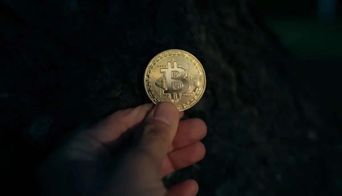 Primo piano di una persona che tiene tra le dita una moneta di Bitcoin dorata; metafora del possesso fisico e del rischio nel mercato peer-to-peer