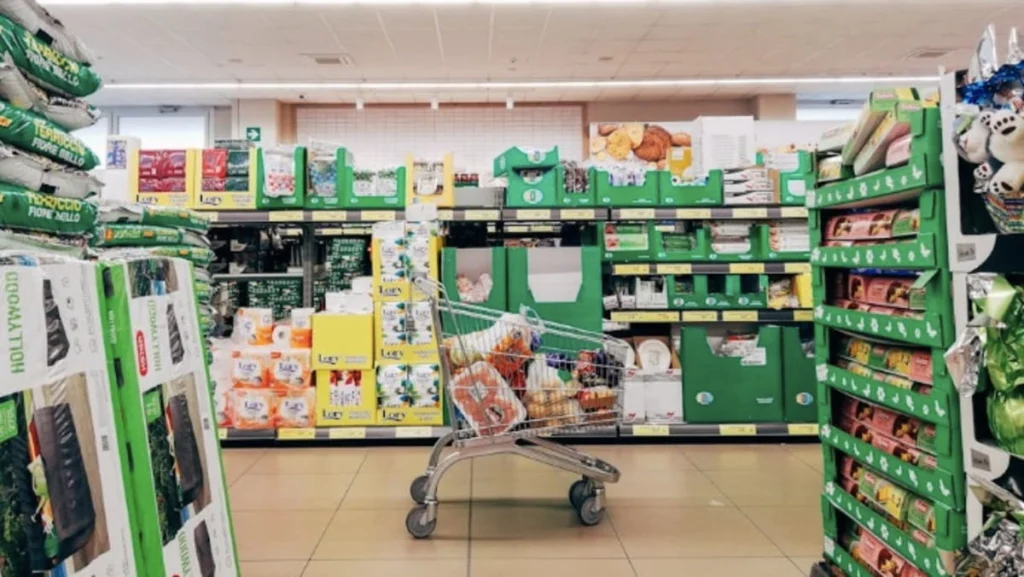 Un carrello della spesa in metallo posizionato lungo la corsia di un supermercato moderno, simbolo di spesa quotidiana per le famiglie