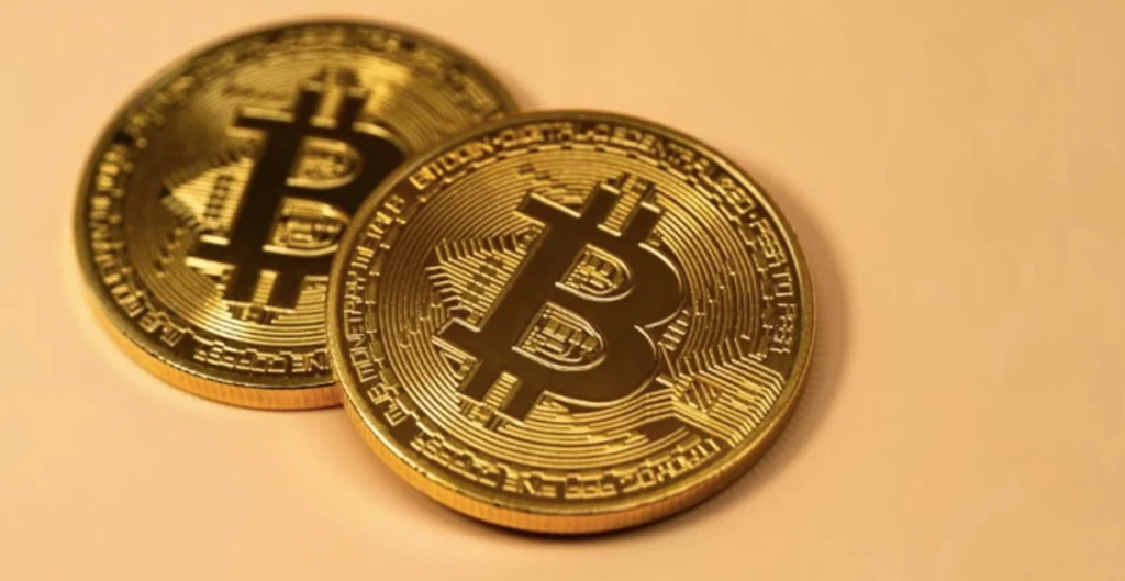 Due monete dorate con il simbolo di Bitcoin affiancate, che rappresentano la rete decentralizzata e il protocollo Proof of Work