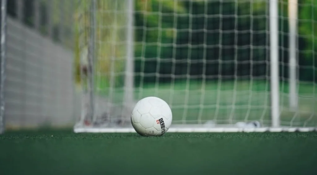 Un pallone da calcio classico adagiato sull'erba verde di un campo sportivo professionale.