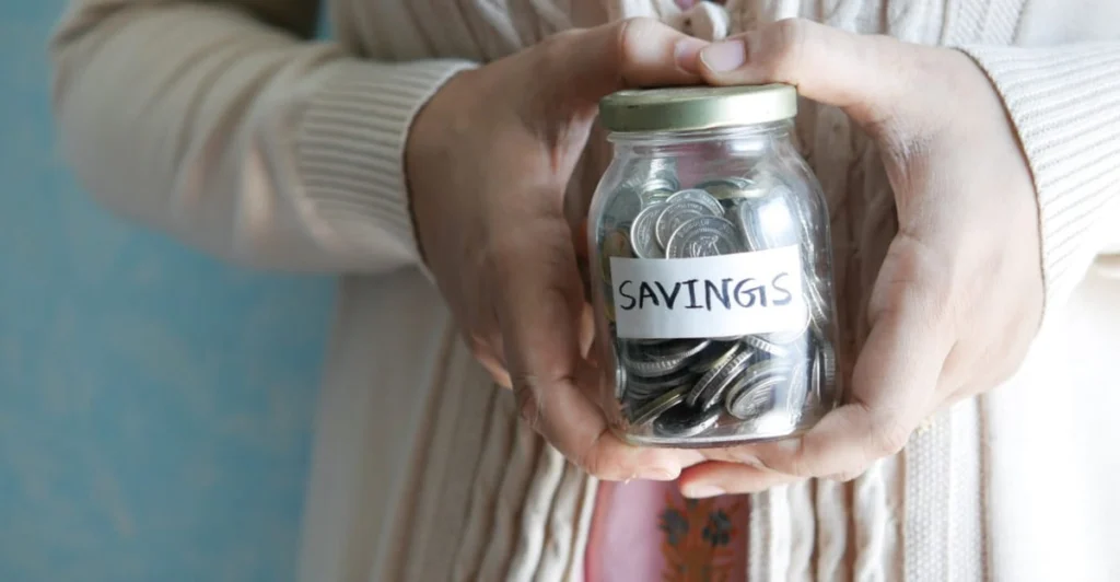 Vasetto di vetro trasparente con etichetta recante la scritta Savings riempito di monete di risparmio