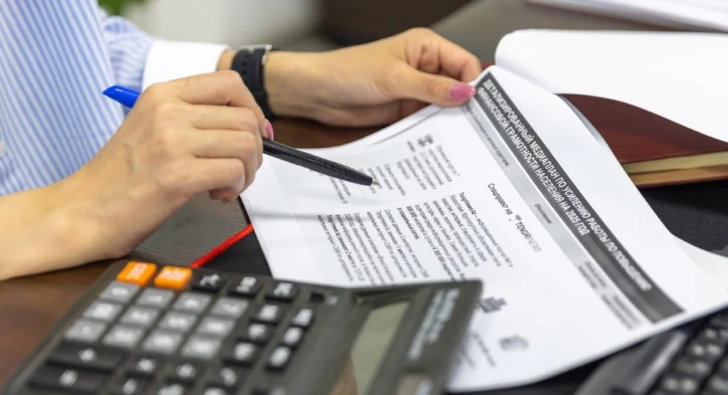 Persona al tavolo mentre consulta documenti fiscali e fatture per il calcolo delle tasse e la richiesta del rimborso IVA trimestrale