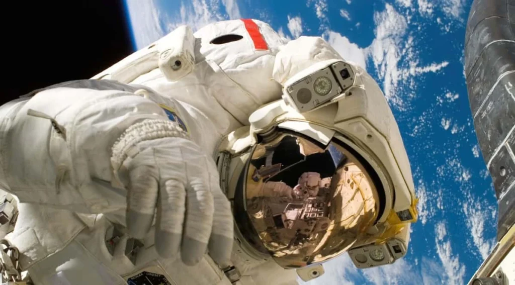 Astronauta con tuta spaziale e visiera riflettente impegnato in una missione in orbita terrestre.